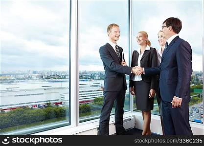 Two businessmen shake hands next to business women