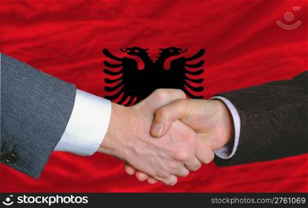 two businessmen shaking hands after good business investment agreement in albania, in front of flag