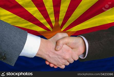two businessmen shaking hands after good business investment agreement in america, in front US state flag of arizona