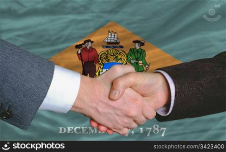 two businessmen shaking hands after good business investment agreement in america, in front US state flag of delaware