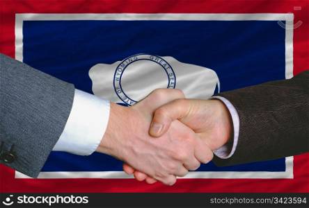 two businessmen shaking hands after good business investment agreement in america, in front US state flag of wyoming