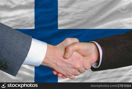 two businessmen shaking hands after good business investment agreement in finland, in front of flag