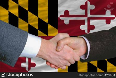 two businessmen shaking hands after good business investment agreement in front US state flag of maryland