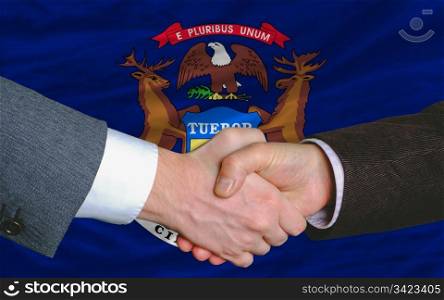 two businessmen shaking hands after good business investment agreement in front US state flag of michigan