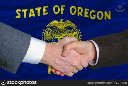 two businessmen shaking hands after good business investment agreement in front US state flag of oregon