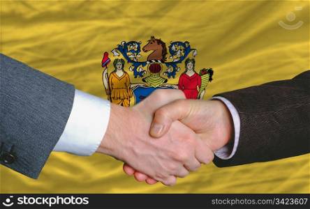 two businessmen shaking hands after good business investment agreement in front US state flag of new jersey