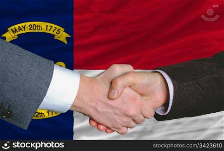 two businessmen shaking hands after good business investment agreement in front US state flag of north carolina