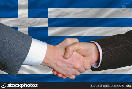 two businessmen shaking hands after good business investment agreement in greece, in front of flag