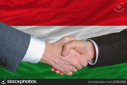 two businessmen shaking hands after good business investment agreement in hungary, in front of flag