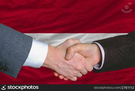 two businessmen shaking hands after good business investment agreement in latvia, in front of flag
