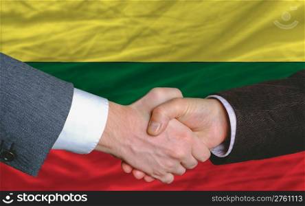 two businessmen shaking hands after good business investment agreement in lithuania, in front of flag