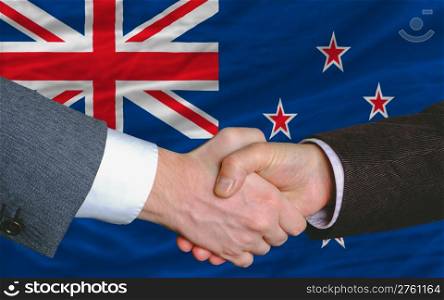 two businessmen shaking hands after good business investment agreement in new zealand, in front of flag