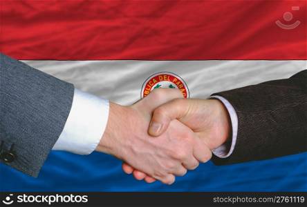 two businessmen shaking hands after good business investment agreement in paraguay, in front of flag