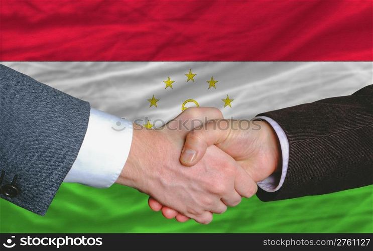 two businessmen shaking hands after good business investment agreement in tajikistan, in front of flag