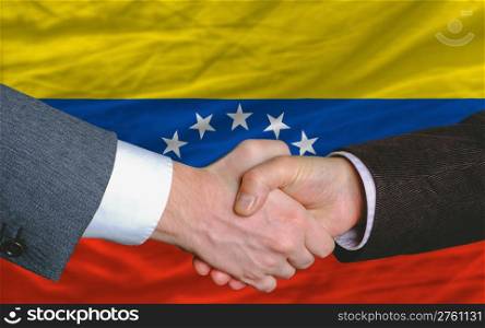 two businessmen shaking hands after good business investment agreement in venezuela, in front of flag