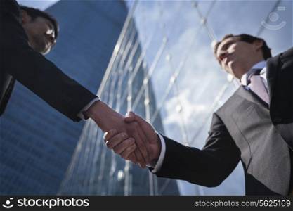 Two businessmen shaking hands in Beijing, China, view from below