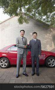 Two Businessmen Shaking Hands Next to Red Car