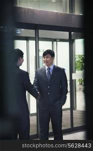 Two businessmen shaking hands, seen through glass wall