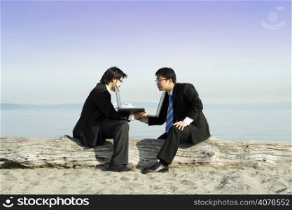 Two businessmen showing their laptops to each other at the beach