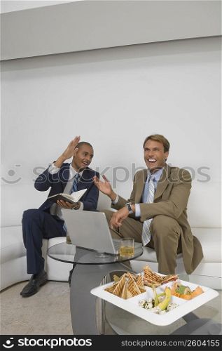Two businessmen sitting in front of a laptop and smiling
