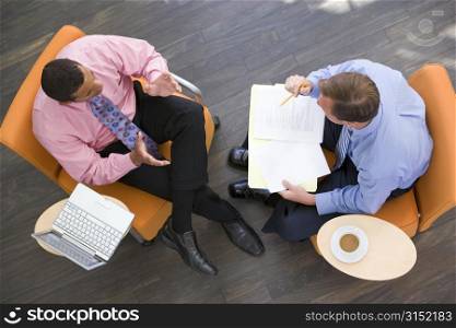 Two businessmen sitting indoors with coffee laptop and folder