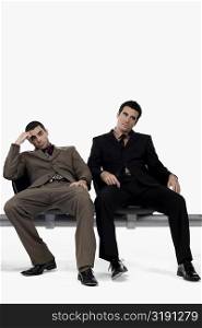 Two businessmen sitting on a bench and looking stressed