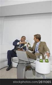 Two businessmen sitting on a couch and celebrating with beer
