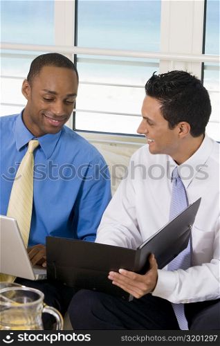 Two businessmen sitting on a couch looking at a file