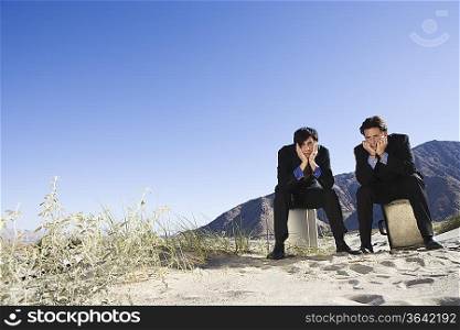 Two Businessmen Sitting on Briefcases in the Desert