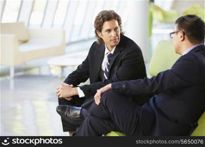 Two Businessmen Sitting On Sofa In Modern Office