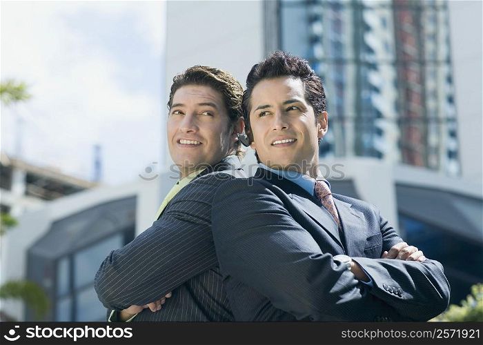 Two businessmen standing back to back and smiling