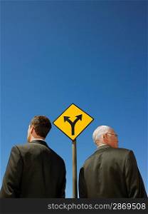 Two businessmen standing by road sign half length back view