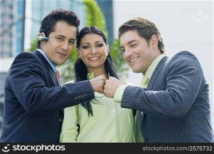 Two businessmen touching knuckles and a businesswoman smiling
