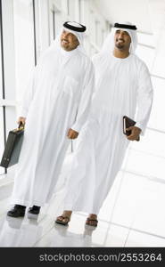 Two businessmen walking in corridor smiling (high key/selective focus)