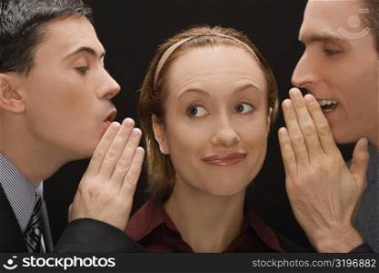 Two businessmen whispering to a businesswoman