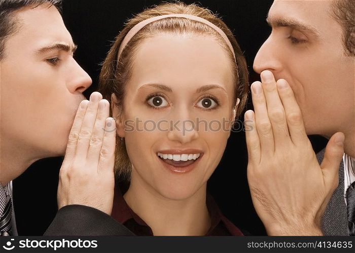 Two businessmen whispering to a businesswoman