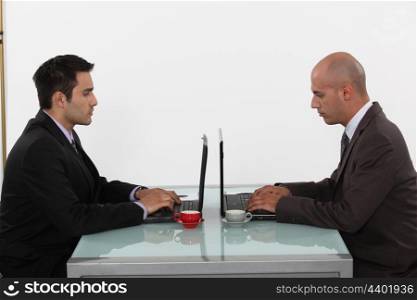 Two businessmen with coffee and laptops