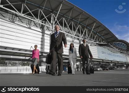 Two businessmen with two businesswomen walking outside at an airport