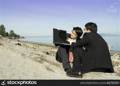 Two businessmen working on their laptop at the beach