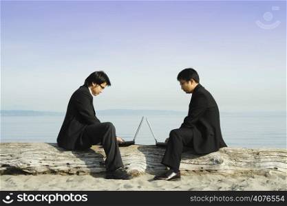 Two businessmen working on their laptops at the beach