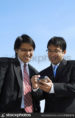 Two businessmen working together looking at a PDA