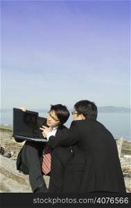 Two businessmen working together with their laptop on the beach