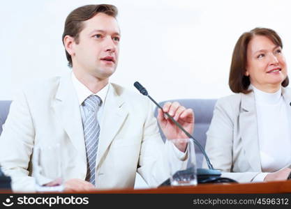 Two businesspeople at meeting. Image of two businesspeople sitting at table at conference speaking in microphone