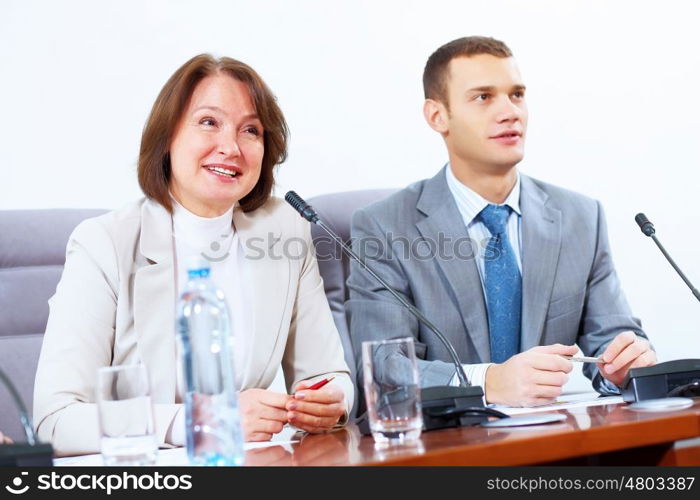 Two businesspeople at meeting. Image of two businesspeople sitting at table at conference speaking in microphone