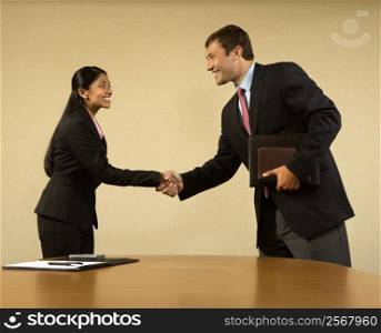 Two businesspeople in suits shaking hands and smiling.