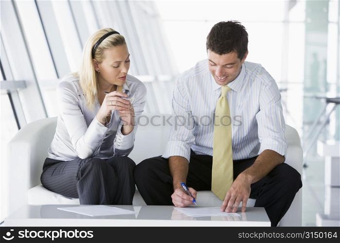 Two businesspeople sitting in office lobby talking and smiling