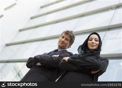 Two businesspeople standing outdoors by building smiling (high key/selective focus)
