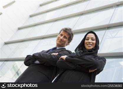 Two businesspeople standing outdoors by building smiling (selective focus)