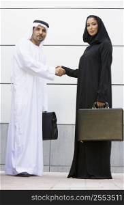 Two businesspeople standing outdoors with briefcases shaking hands