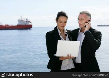 Two businesspeople stood with a laptop by the coast